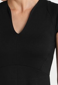 Abito nero con scollo a V e maniche corte. Realizzato in tessuto liscio, presenta un corpetto aderente e dettagli delle cuciture. Design semplice e classico.