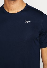 Mörkblå kortärmad sporttröja i mjukt tyg, med en vit logotyp på övre vänstra bröstet och rundad halsringning.