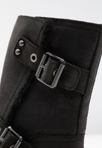 Černé semišové boty s kovovým stříbrným přezkovým páskem, cvočkovými detaily a měkkou, plyšovou podšívkou na vrchní části.