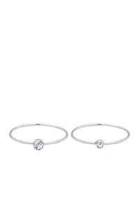 Dos anillos de plata con una banda delgada y una única piedra clara engastada en un bisel en el centro de cada anillo. Diseño simple y moderno.