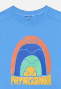 Šviesiai mėlynas trumpas rankovės marškinėliai, kuriuose yra daugiaspalvė geometrinė dizaino kompozicija su arkų motyvais ir žodžiu "PATAGONIA" paryškintu tekstu apačioje.