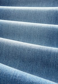 Zbliżenie złożonego, jasnoniebieskiego materiału dżinsowego pokazującego diagonalną teksturę tkania i miękkie cienie.