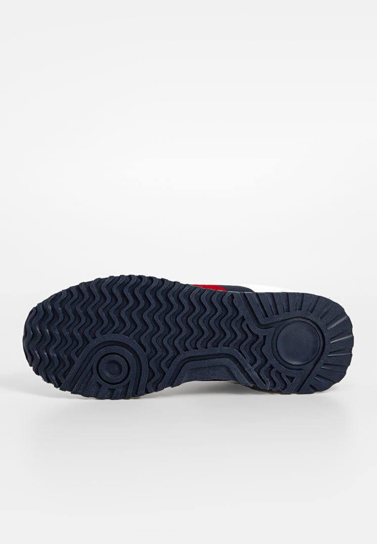 Suola della scarpa con una base in gomma blu navy solida, caratterizzata da un motivo del battistrada ondulato e accenti di presa circolari; evidenzia elementi di design rossi sui lati.