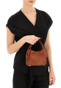 Borsa a mano in pelle marrone con una forma rotonda, caratterizzata da accessori in metallo dorato e una morbida texture, tenuta da una persona in un outfit nero.