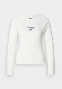 Cămașă albă cu mâneci lungi și design ajustat, cu margine brută, decolteu rotund și logo "tommy girl" în culoarea albastru marin. Material moale.