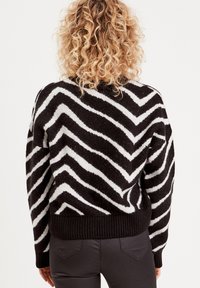 Pull à motif chevron noir et blanc avec une finition texturée, doté d'un ourlet et de poignets côtelés, vu de l'arrière.