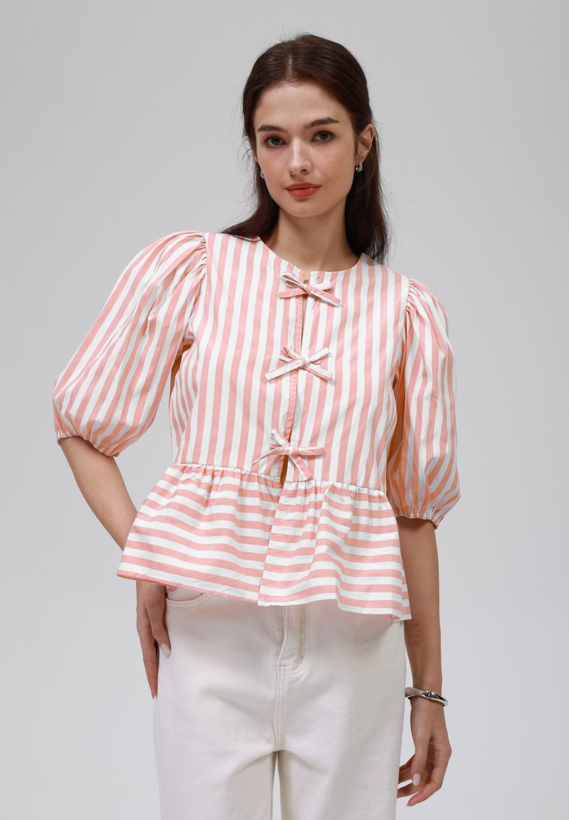 Peplum-Bluse mit rosa-weißen vertikalen Streifen, verfügt über Puffärmel, drei Schleifenakzente und einen runden Ausschnitt. Kombiniert mit weißen Hosen.