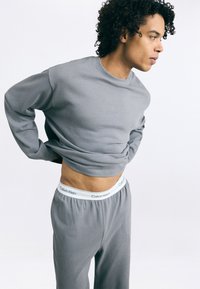 Šedá bavlněná mikina a odpovídající tepláky mají žebrovaný límec a elastický pas se zvýrazněním bílým logem Calvin Klein.