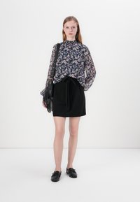 Blomstermønstret, gjennomsiktig bluse med lange ermer; svart skjørt med knyttet midje; kombinert med svarte slip-on sko og en frynset håndveske.