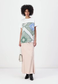 T-shirt blanc avec un motif vert et bleu à l'avant, associé à une jupe maxi rose pâle comportant des boutons sur le côté et une finition élégante.