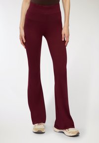 Burgundowe spódnice w kształcie dzwonu wykonane z elastycznego materiału, z wysokim pasem i gładką teksturą. Noszone z jasnymi butami sportowymi.