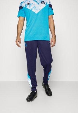 Ensemble de sport bleu et marine, comprenant un t-shirt à manches courtes avec un motif nuage et un logo, associé à un pantalon fuselé assorti et des chaussures noires.