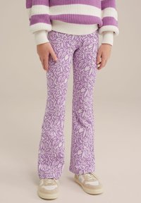 Pantaloni a zampa d'elefante viola con un motivo floreale bianco, realizzati in un tessuto morbido. Abbinati a sneakers beige con dettagli bianchi.