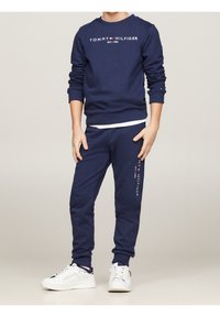 Granatowy zestaw dresowy z bluzą i spodniami z logo "Tommy Hilfiger", ściągaczami u dołu oraz dopasowanymi białymi sneakerami o teksturowanej powierzchni.