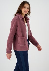 Giacca in pile color rosa polveroso, con colletto, zip frontale e tasca a toppa con bordo a contrasto. Tessuto morbido e vestibilità rilassata.