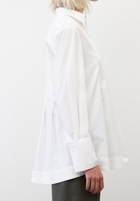 Camisa blanca de manga larga en algodón ligero, con un cuello clásico, dobladillo curvado y un ajuste holgado con puños abotonados.