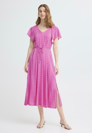 Naine kannab roosat mustrilist midi-kleiti lehvivate varrukate ja küljetõmbeauguga, seisab ühevärvilise heleda tausta ees.