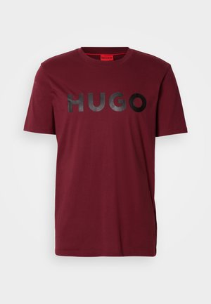 Bordeaux-rotes T-Shirt mit kurzen Ärmeln und glänzendem schwarzen "HUGO"-Logo auf der Brust vor einem einfachen hellen Hintergrund.