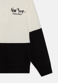 Felpa nera e crema con logo ricamato "New York" e "Calvin Klein", con polsini a coste e design a blocchi di colore.