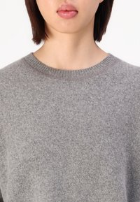 Grå tröja med rund halsringning, tillverkat av mjukt stickat tyg. Slät yta, har en minimalistisk design utan mönster eller utsmyckningar.