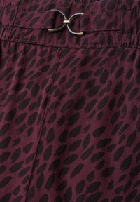 Burgundy fabric with black animal print pattern featuring a stitched seam and a decorative tortoiseshell double ring buckle.