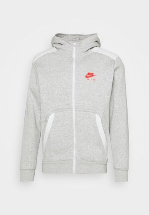 Haut à capuche zippé gris avec une capuche, accents blancs sur les épaules, logo rouge Nike Air sur la poitrine et deux poches avant. Texture de tissu douce.