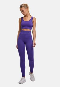 Fioletowy komplet sportowy składający się z biustonosza i legginsów. Biustonosz ma głęboki dekolt, a legginsy posiadają teksturowane panele oraz wysoki pas.