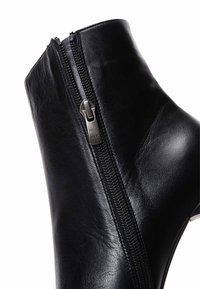 Bottine en cuir noir avec fermeture éclair latérale, texture lisse et élégante, légèrement brillante et au design minimaliste.