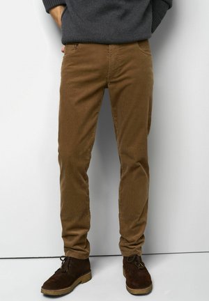Pantalons en velours côtelé marron clair avec une coupe droite, dotés de poches latérales, d'une fermeture éclair et associés à des chaussures en daim marron foncé.