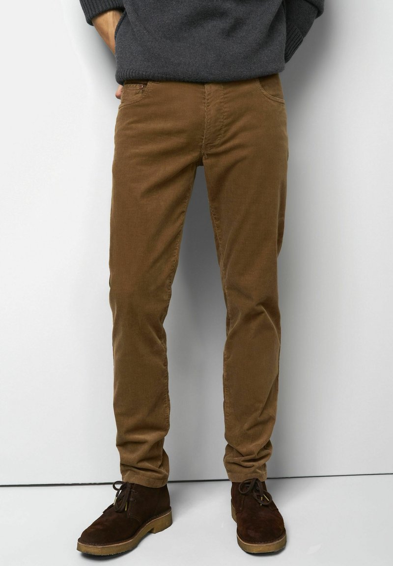 Pantalons en velours côtelé marron clair avec une coupe droite, dotés de poches latérales, d'une fermeture éclair et associés à des chaussures en daim marron foncé.