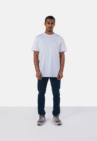 T-shirt blanc à col rond avec des manches courtes, associé à un pantalon bleu marine et des baskets grises. Le t-shirt présente un détail de logo discret.