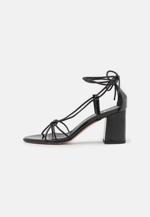 Schwarze Lackleder High-Heel-Sandalen mit quadratischer Zehenpartie, Knöchelriemen und Knoten-Verzierung. Blockabsatz-Design für Stabilität.