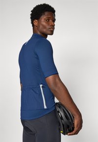 Maillot de cyclisme navy à manches courtes, design ajusté, poche arrière et accents réfléchissants. Texture lisse, associé à un casque noir.