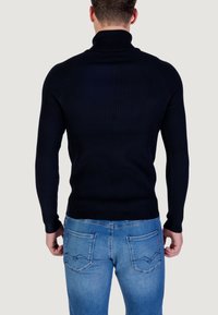 Maglione a collo alto navy a costine con maniche lunghe, abbinato a jeans azzurri chiari con tasche posteriori e dettagli di cucitura sottili.