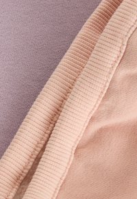 Dwa próbki tkanin: jedna lawendowa dzianina i jedna brzoskwiniowa tkanina ribbed, prezentujące gładkie i miękkie tekstury w kontrastujących kolorach i wykończeniach.