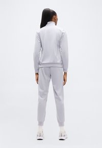 Ανοιχτό γκρι αθλητικό σύνολο με ζακέτα με φερμουάρ και αντίστοιχο κολάν με στενή εφαρμογή. Διαθέτει ριμπ μανσέτες και μαλακή, λεία υφή.