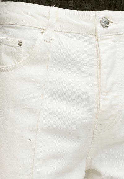 Κοντινό πλάνο λευκών τζιν από denim που δείχνει μπροστινή τσέπη, θηλιά ζώνης, ραφές και κλείσιμο με ασημί μεταλλικό κουμπί.