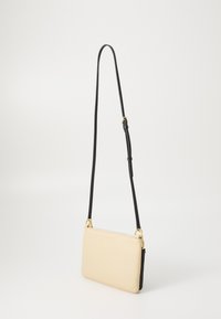 Borsa a tracolla beige in pelle con una lunga tracolla nera regolabile e dettagli in oro, appoggiata su uno sfondo bianco semplice.
