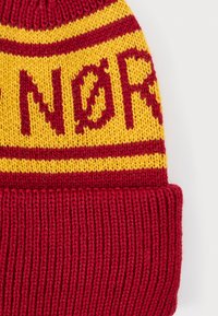 Bonnet tricoté rouge et jaune avec un motif de rayures horizontales, affichant le mot "NØR" en lettres rouges en gras sur une bande jaune.