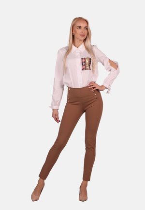 White button-up shirt with a patterned pocket, paired with brown high-waisted pants featuring side buttons and a fitted silhouette.