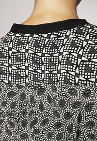 Černobílý vzorovaný oděv s geometrickými a paisley vzory. Textura je hladká s kontrastním černým límcem.