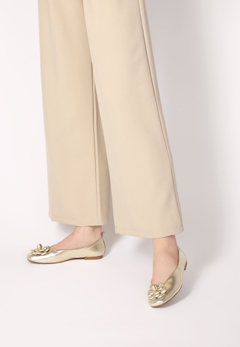 Goldene metallic Ballerinas mit runder Zehenpartie, die vorne mit einem floralen Akzent verziert sind. Der Schuh hat eine flache Sohle und ein minimalistisches Design.