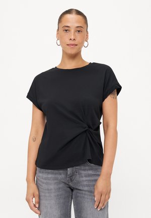 Black short-sleeve t-shirt with a knotted front design, made of soft fabric. Worn with light gray jeans. Simple round neckline.
