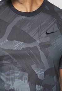 Camiseta Nike en negro y gris con patrones abstractos de pinceladas, manga corta y cuello redondo, con un pequeño logo en el pecho.