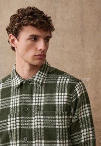 Groen-wit geruit overhemd met kraag, voorzien van een knoopsluiting aan de voorkant, traditionele flanellen textuur en een borstzak aan de linkerkant.