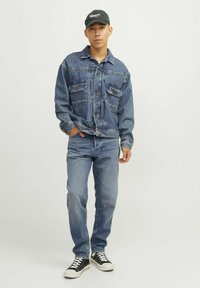 Jachetă din denim cu două buzunare pe piept, albastră, croi lejer; asortată cu blugi albaștri deschisi și adidași negri cu accente albe. Capac negru.