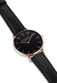 Reloj redondo negro con caja dorada, esfera negra, marcadores de hora dorados y correa de cuero negro. Nombre de la marca "Victoria Hyde London" visible.