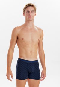 Námořnické modré boxerky se šachovnicovým vzorem, s modrým pasem a značkou "JSS Underwear". Hladká textura a přiléhavý design.