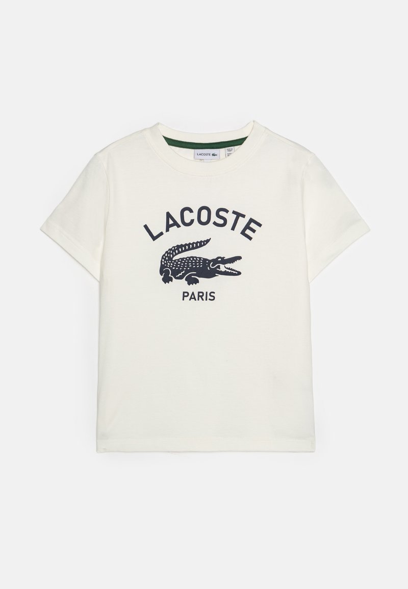 Hvit bomull t-skjorte med korte ermer, med en marineblå krokodillelogo og "LACOSTE PARIS" tekst i fet skrift.