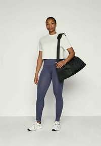 Borsa a tracolla nera, maglietta corta grigia chiara, leggings blu navy a coste e sneakers bianche. L'outfit presenta una vestibilità comoda e un design sportivo.